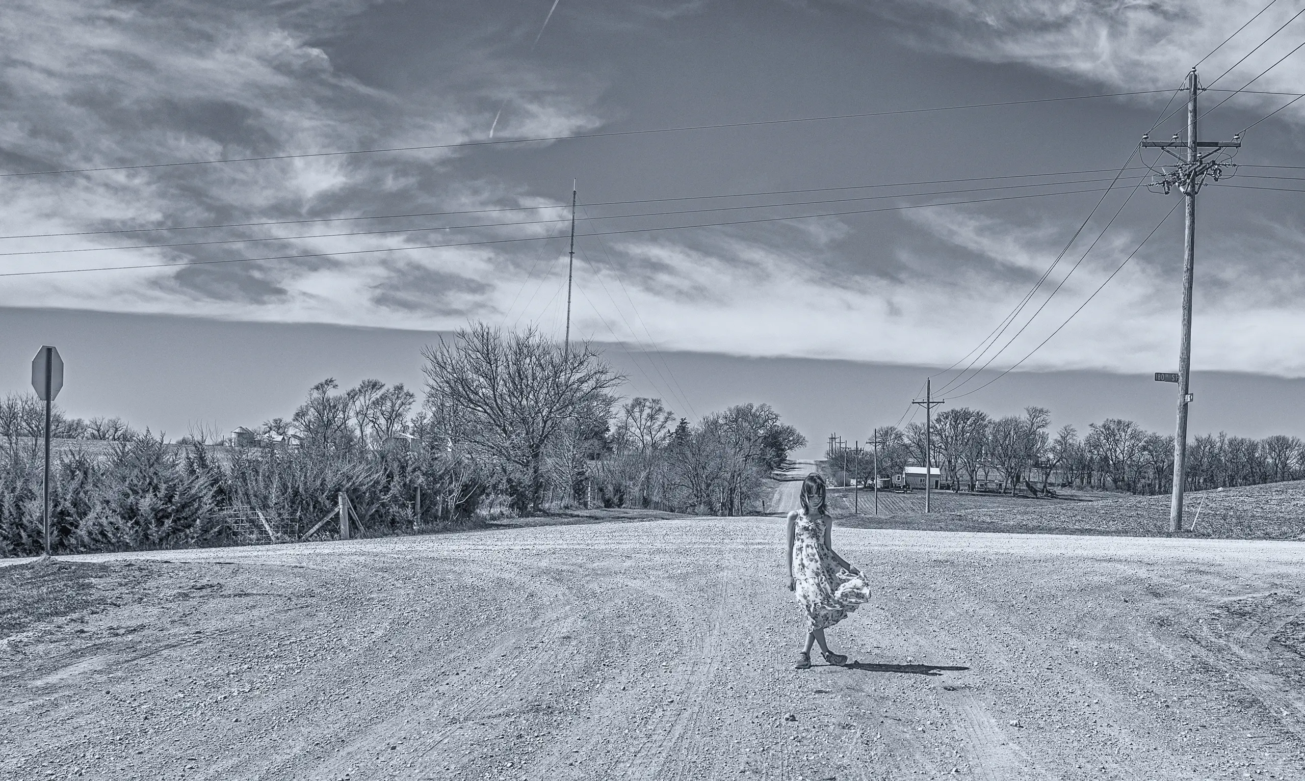 Brooklyn Mitchell, age nine, standing alone at a dirt crossroads in a sundress. Black and white.